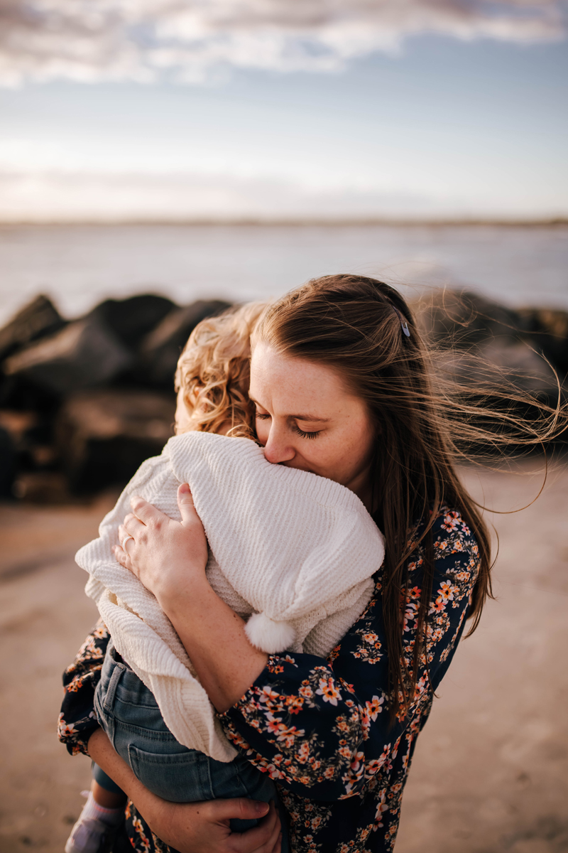 mother cuddling into baby girl on chilly beach morning at sunrise