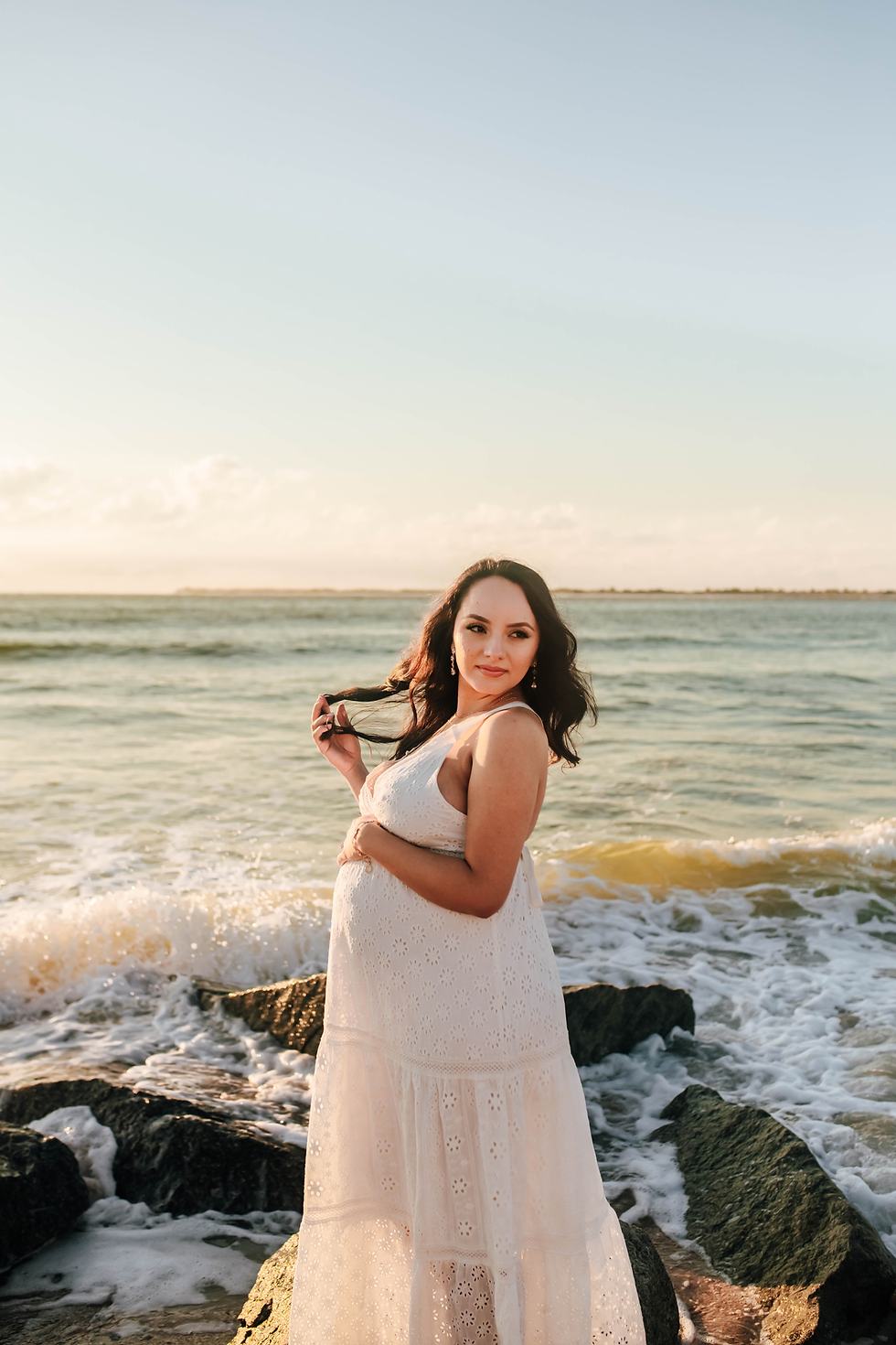 expecting mother in white dress on rocky beach at sunrise