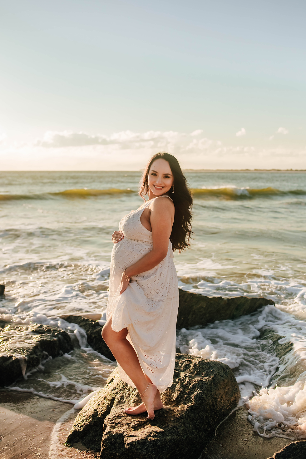 expecting mother standing on rock during sunrise beach photoshoot