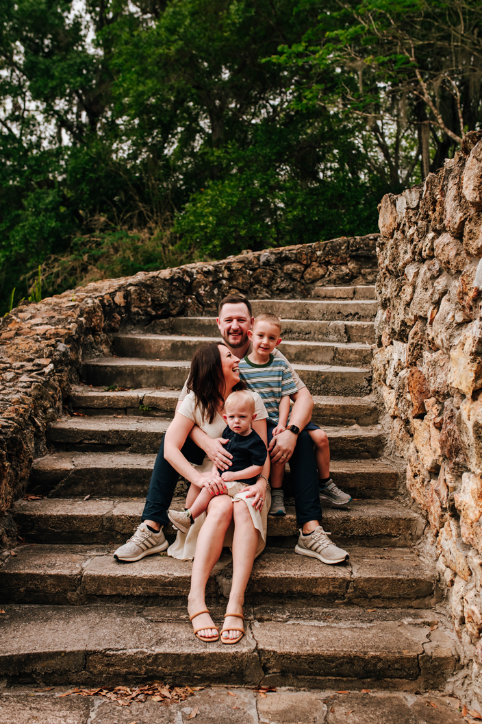 family together sitting on rock staircase in historic state park during family photos