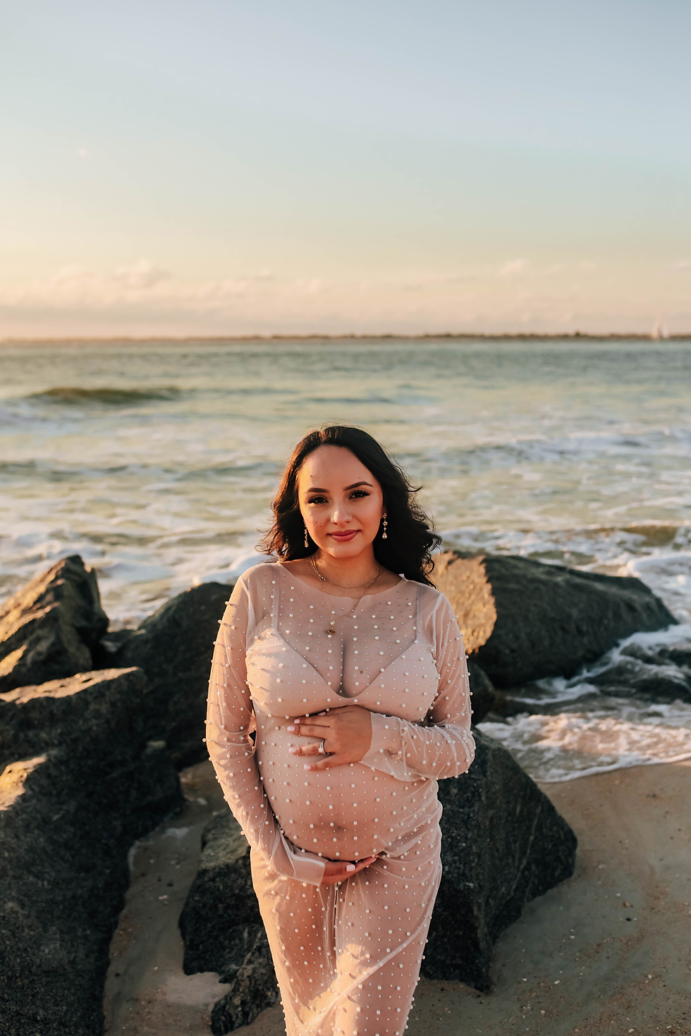 smiling pregnant mother on rocky beach during sunrise photoshoot