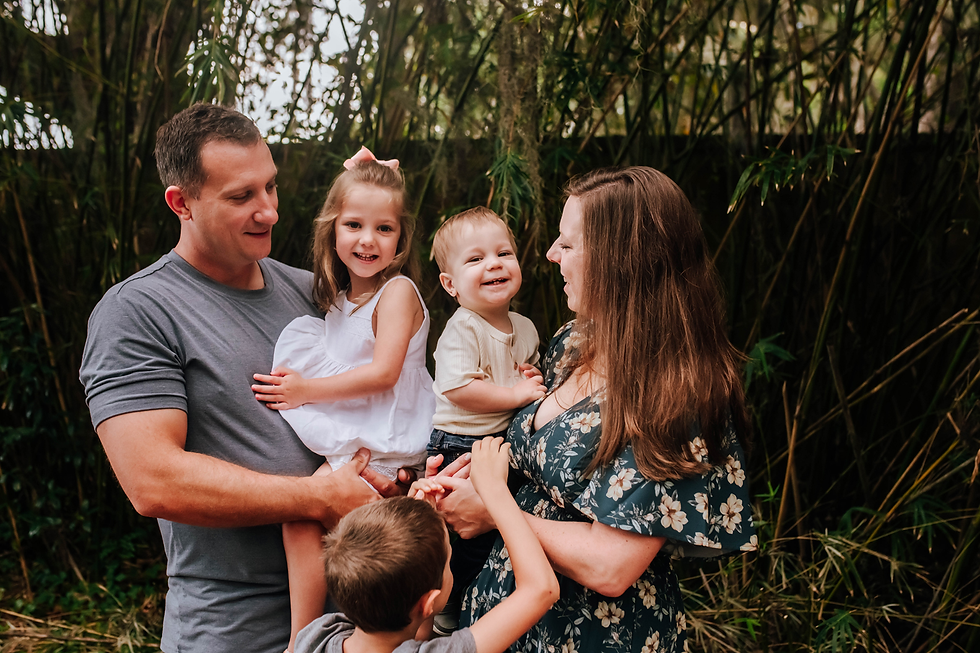 older brother tickles baby brother in mom's arms while dad holds sister during a recent family photography session