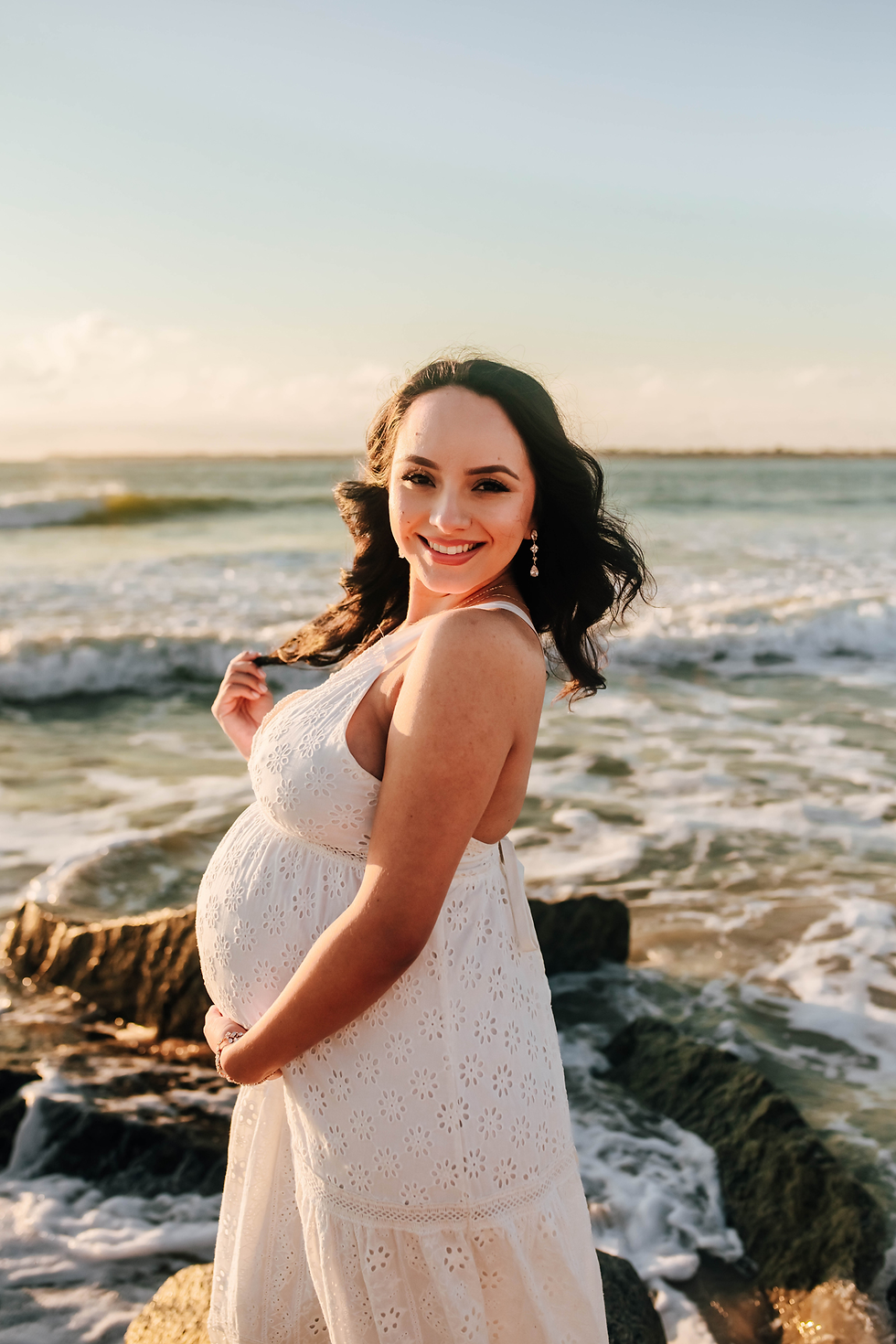 smiling pregnant woman on rocky beach during maternity photos
