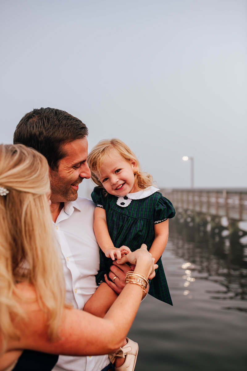 parents tickle toddler girl on a foggy pier during maternity photos