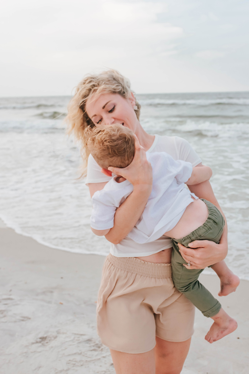 mother looks at son as she twirls him around during beach family photoshoot