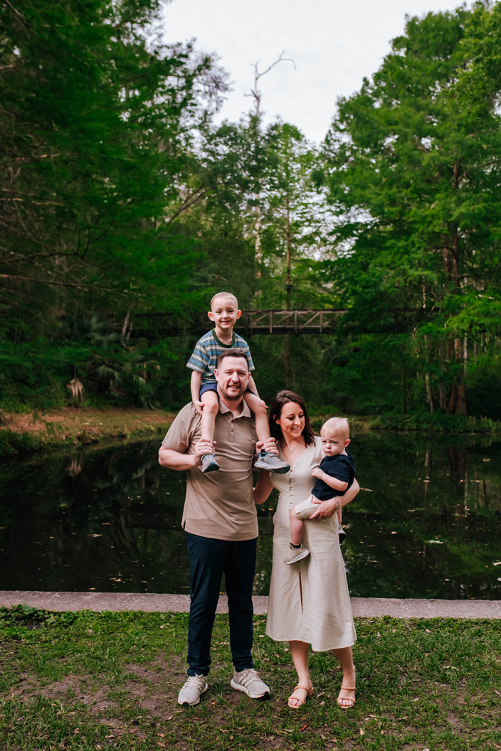 mom holds youngest son while oldest sits on dads shoulders during state park family portraits