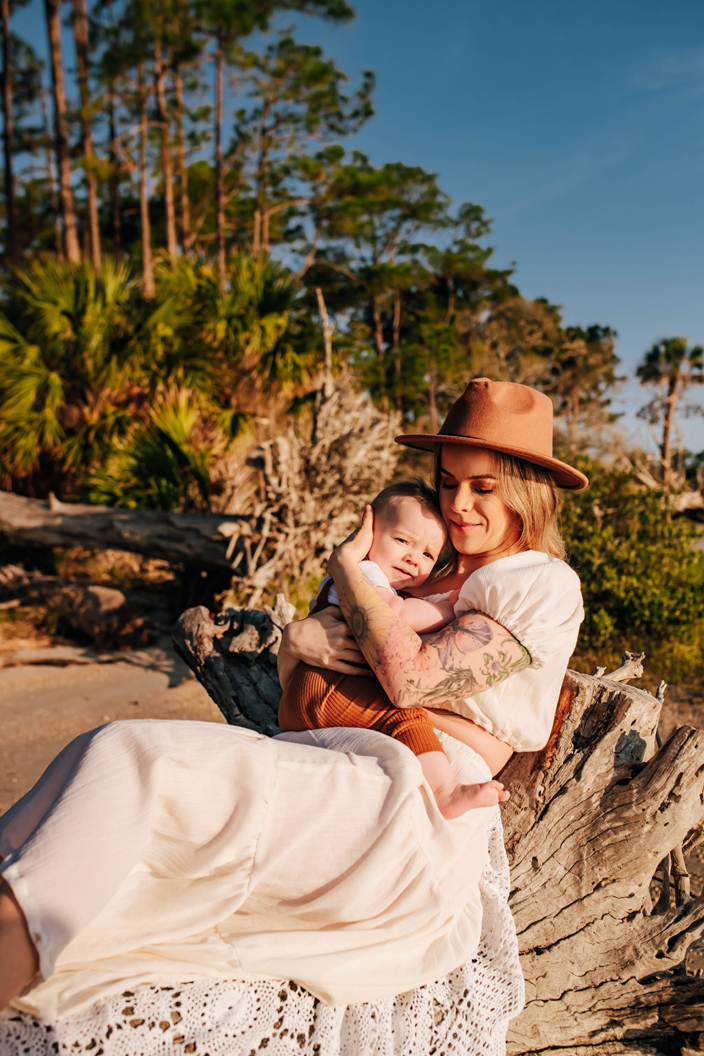 mother sitting on fallen driftwood tree holding her baby boy during family photoshoot