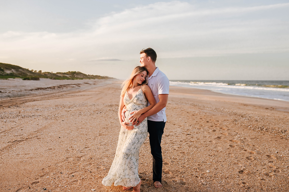 couple cuddles in close as husband kisses the top of her head during beach maternity pictures
