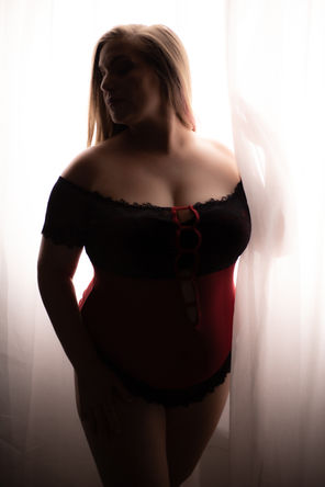 Beautiful plus sized woman stands in a window wearing lingerie in our boudoir studio