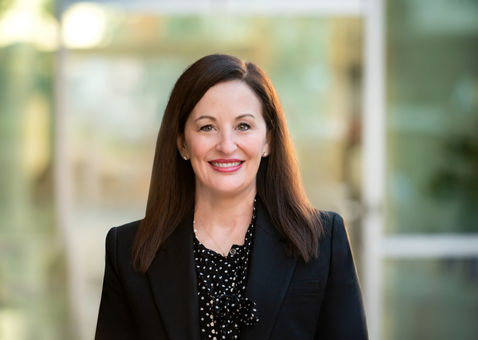 Modern headshot of woman in white blazer smiling confidently in natural light near The Star in Frisco, TX.