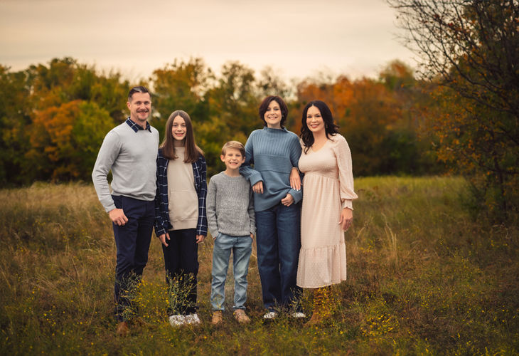 Frisco family photographer documents parents holding hands with their kids while walking through a sunlit field