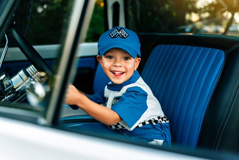 a milestone session for third birthday wear little boy is dressed in a blue race car driver sitting in a truck that matches his blue and black outfit. 