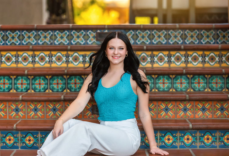High school senior sitting on steps in downtown Frisco wearing casual jeans and a confident smile.