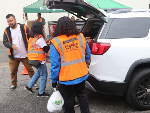 Food bank volunteers loading donated food into recipients' cars.