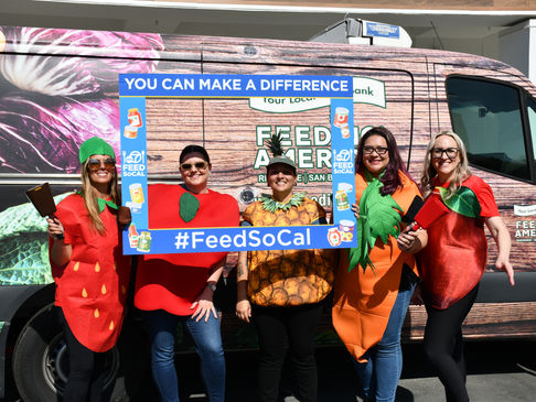 Group of people wearing fruit costumes holding a frame with text, "Feed SoCal."
