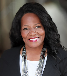 Professional headshot of woman with brown hair wearing a black blazer shot in natural light in New York City