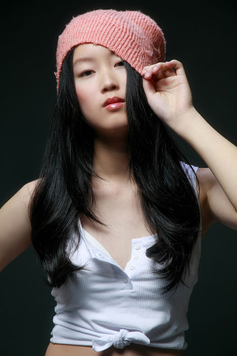 Young Asian fashion model shot in studio with dramatic light, wearing a pink hat and white shirt against a black background