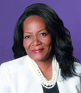 Corporate headshot of black female executive wearing white suit in front of purple background