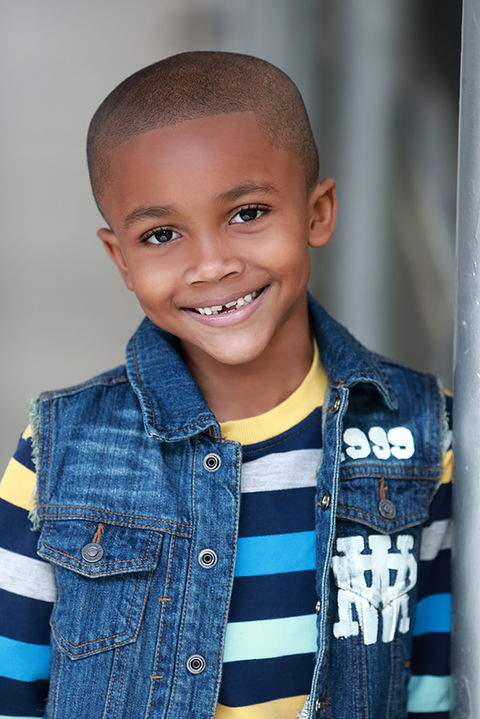 Actor headshot of a smiling young boy wearing a denim vest shot in studio with natural light and blurred background