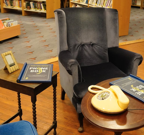 Armchair, side tables, a yellow telephone and a photograph.