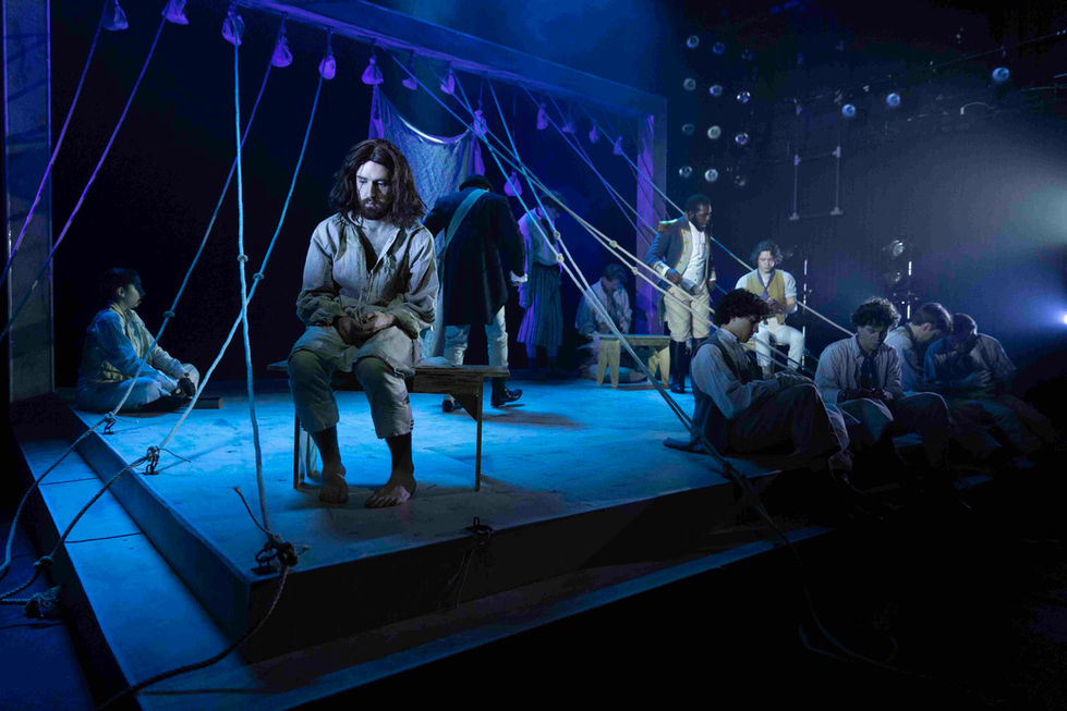 A production photo of the cast sat on stage
