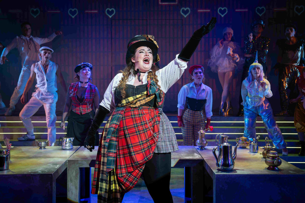 A production photo of a lead actress singing around tables covered in teapots