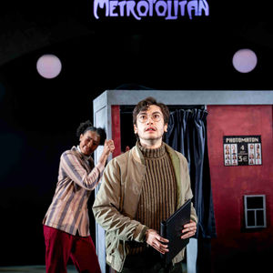 A production photo of the male lead standing outside of a photobooth.