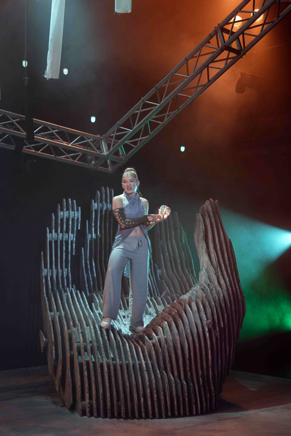 A production photo of an actress standing on the hand sculpture.