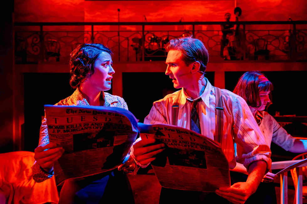 A production photo of some actors reading a newspaper