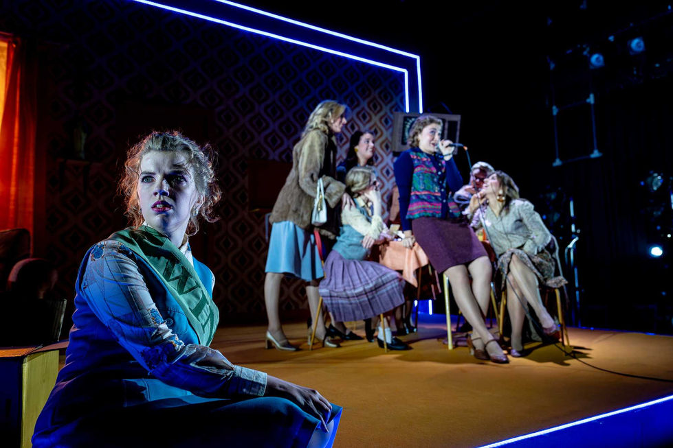 A production photo where the main character is off to the side as the ensemble is gathered.