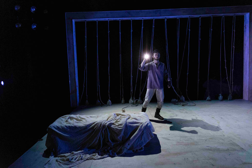 A production photo of an actor with a torch on stage
