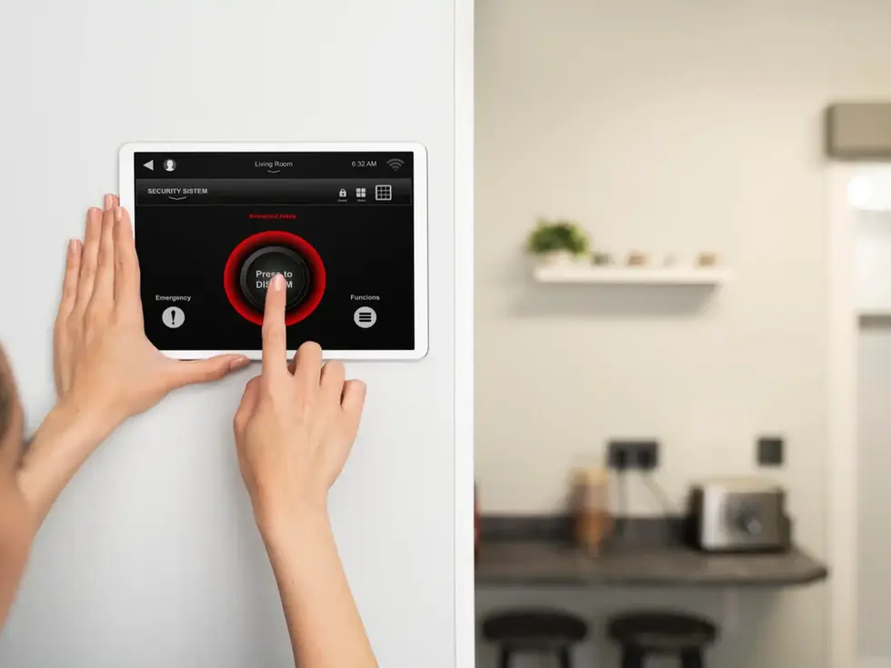 Hands operating wall-mounted tablet displaying "Security System ARM STAY ARM AWAY".
