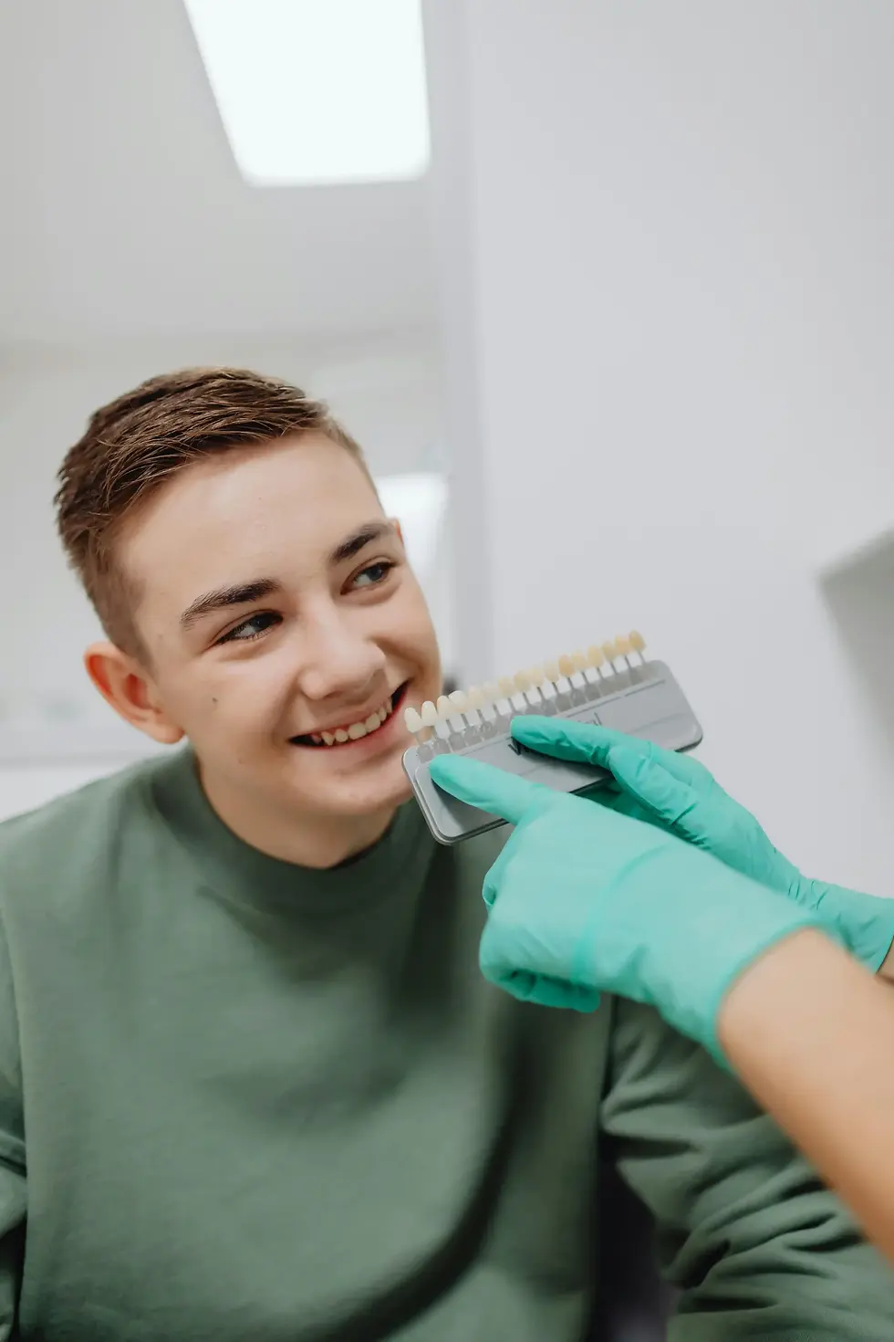 Smiling man getting tooth color matched by gloved dentist.