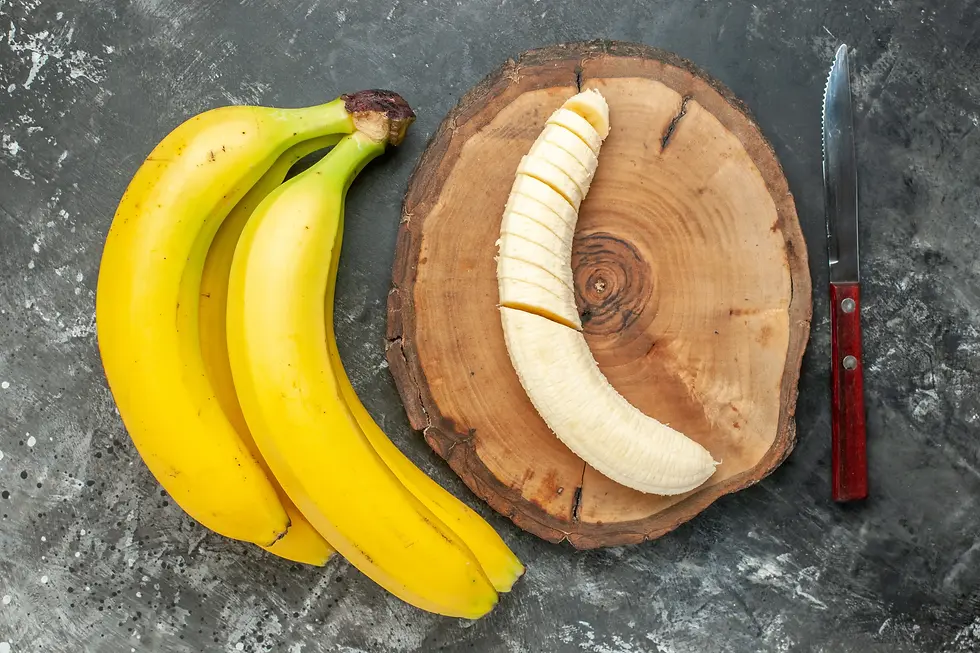 Sliced banana on wooden board, two whole bananas beside