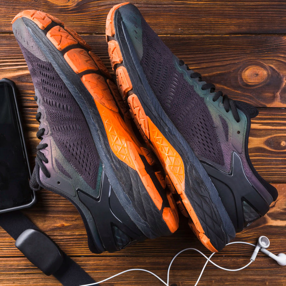 Pair of black and orange running shoes on wooden background with accessories.