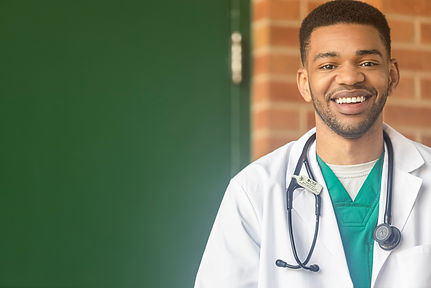 Smiling healthcare professional wearing green medical scrubs, a white lab coat, and a stethoscope during a professional environmental headshot inside a modern healthcare facility. Ideal for hospital websites, physician profiles, medical practice branding, healthcare marketing, and LinkedIn.
