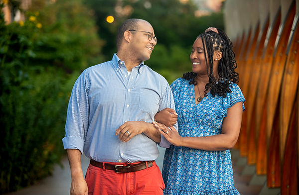 Romantic Chicago engagement photo of couple walking arm in arm in a garden setting, smiling at each other with soft natural light and greenery backdrop