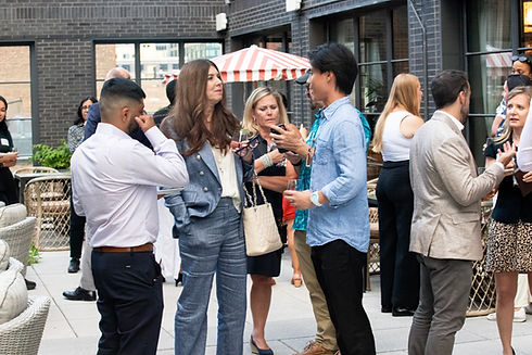 Event sponsor speaks with guests during an outdoor networking mixer at Cira at The Hoxton Chicago in the West Loop, as groups of professionals socialize throughout the terrace.