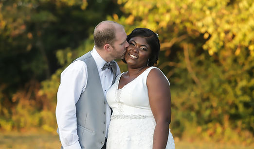 Golden hour wedding portrait of the groom kissing the bride’s cheek during a warm sunset moment.