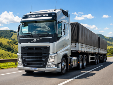 A imagem mostra um caminhão grande e moderno, semelhante a um Volvo FH 540, rodando em uma estrada asfaltada bem conservada. O caminhão é prateado, com cabine alta e design robusto. Na parte frontal, dá pra ver detalhes como a grade grande, faróis modernos e o nome “Globetrotter” no topo da cabine. Ele está puxando uma carreta longa, coberta por uma lona preta, indicando transporte de carga.