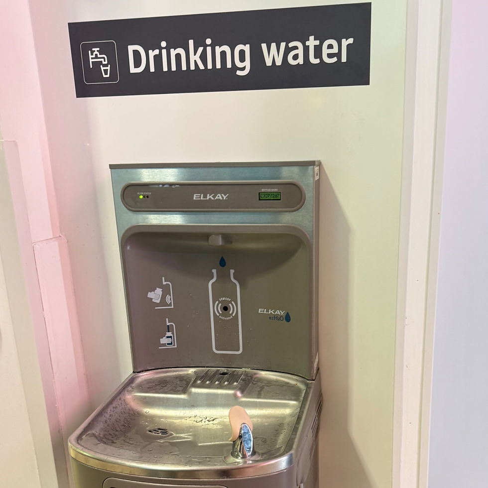 Passenger filling a refillable bottle at free water fountain inside Luton Airport terminal