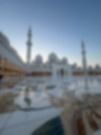 White mosque with domes and minarets at sunset, intricate floral patterns on courtyard tiles. Calm and serene atmosphere. Top 5 Things to Do in Abu Dhabi