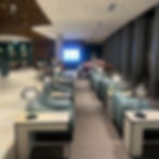 Modern lounge with teal chairs and side tables with stylish lamps. Large screen at the back displays ads. Calm, upscale ambiance. Vienna Airport Lounge – The Best in the World?