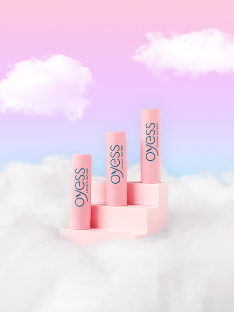 Fotografie von drei Oyess Lippenpflegestiften, die im Himmel, auf rosa Treppen stehen.
Photograph of three Oyess lip balms standing in the sky, on pink stairs.