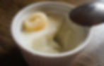 A spoon scooping into soft almond jelly with a single longan resting on top, inside a white ramekin.