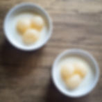 Top view of two ramekins filled with smooth almond jelly topped with canned longan fruits on a wooden surface.
