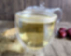 Glass cup of freshly brewed osmanthus red date tea with dried blossoms and red dates in the background.