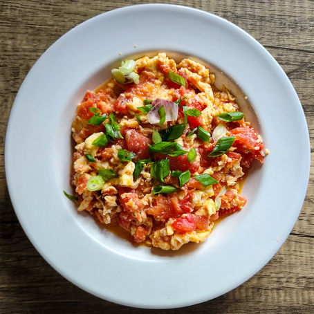 Chinese tomato egg stir fry with fluffy scrambled eggs and softened tomatoes in a rich, chunky sauce, garnished with fresh scallions and served over rice.