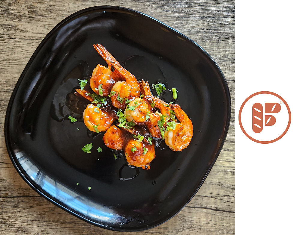 Black plate of grilled prawns with honey glaze and chopped herbs, photographed from above.