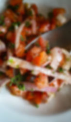 Top-down photo of tomato onion salad in a white bowl on a wooden surface.